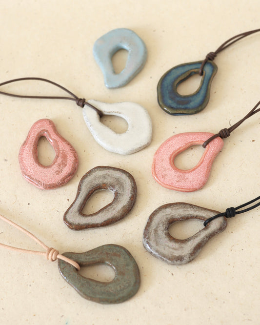 Hand-shaped, ceramic, light grey speckled stoneware amulet hanging from a black leather cord, worn as a subtle statement piece.