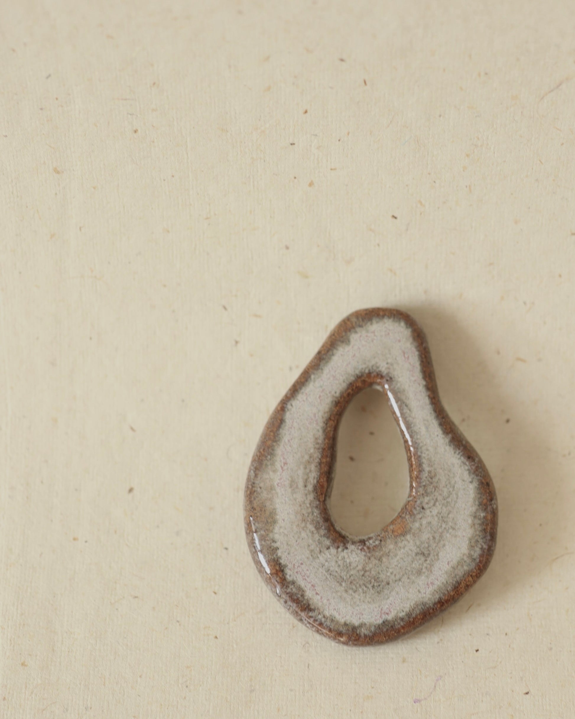 Light grey, hand-formed speckled stoneware amulet finished with two different glazes, showing subtle speckling and smooth contours.
