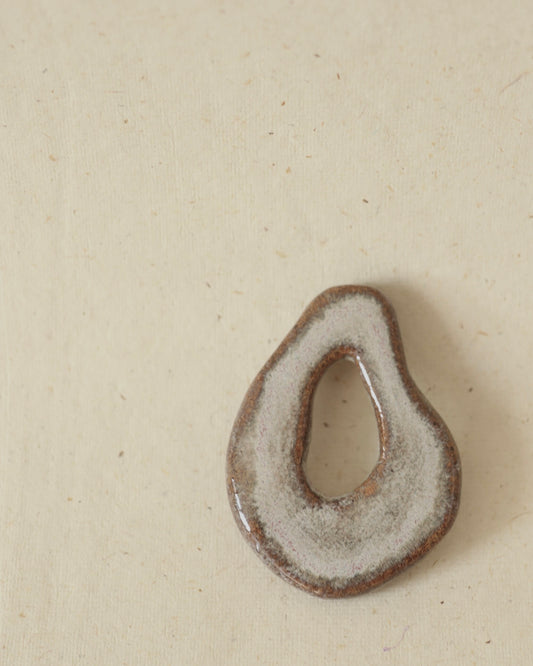 Light grey, hand-formed speckled stoneware amulet finished with two different glazes, showing subtle speckling and smooth contours.