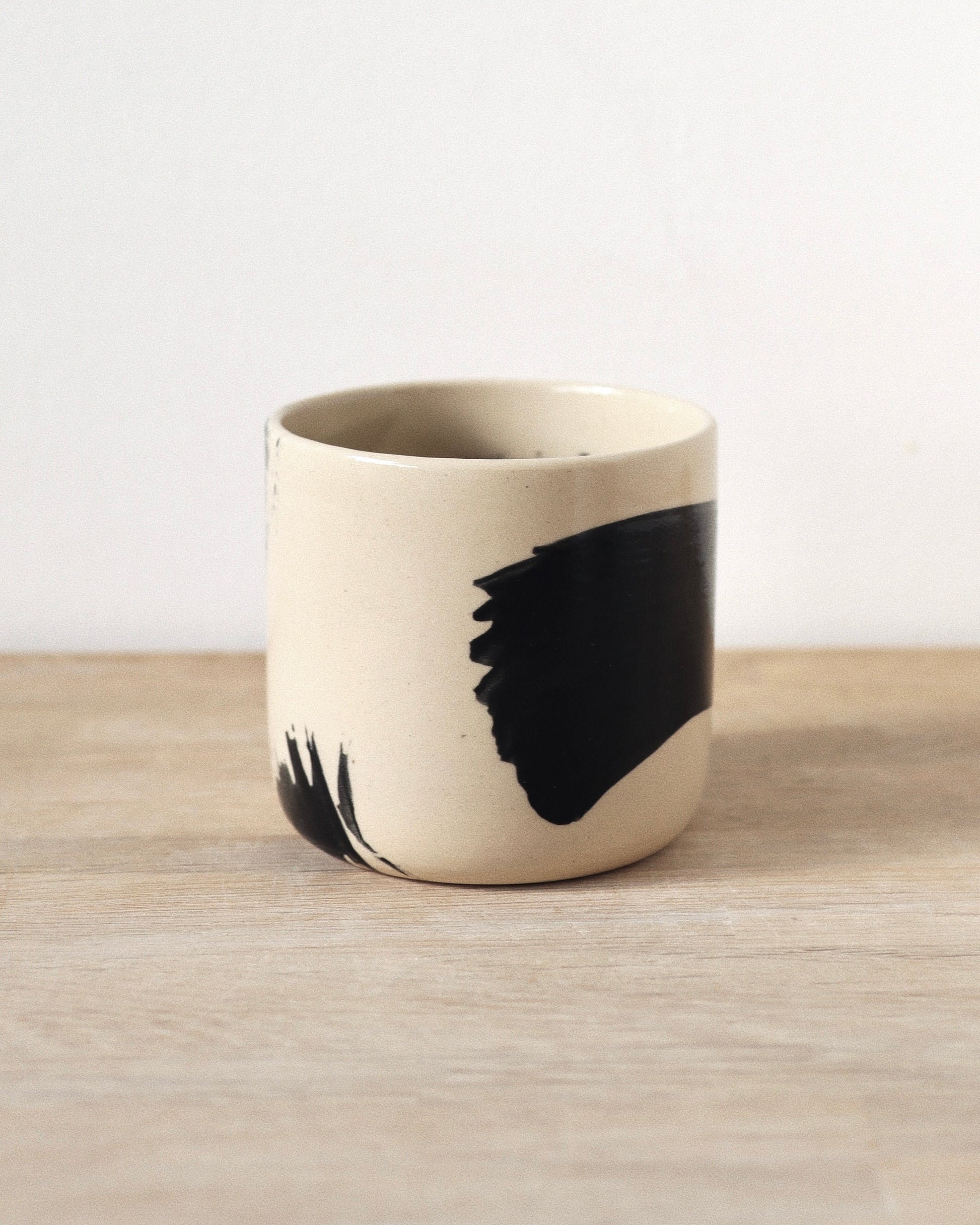 Brush-Stroked Clear Cup – handmade wheel-thrown white stoneware cup with expressive black brushstrokes and a clear glaze, crafted in Amsterdam by Zeyah Ceramics.