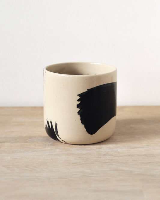 Brush-Stroked Clear Cup – handmade wheel-thrown white stoneware cup with expressive black brushstrokes and a clear glaze, crafted in Amsterdam by Zeyah Ceramics.