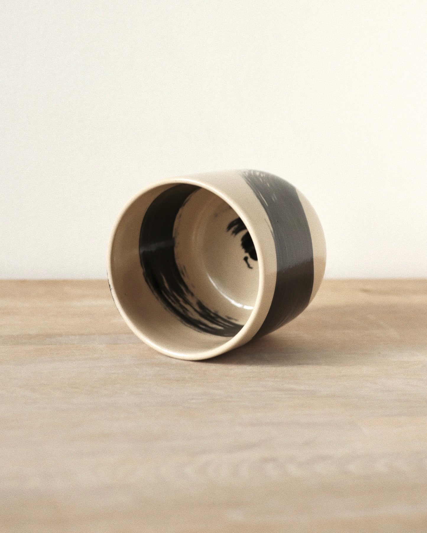 Brush-Stroked Clear Cup – handmade wheel-thrown white stoneware cup with expressive black brushstrokes and a clear glaze, crafted in Amsterdam by Zeyah Ceramics.