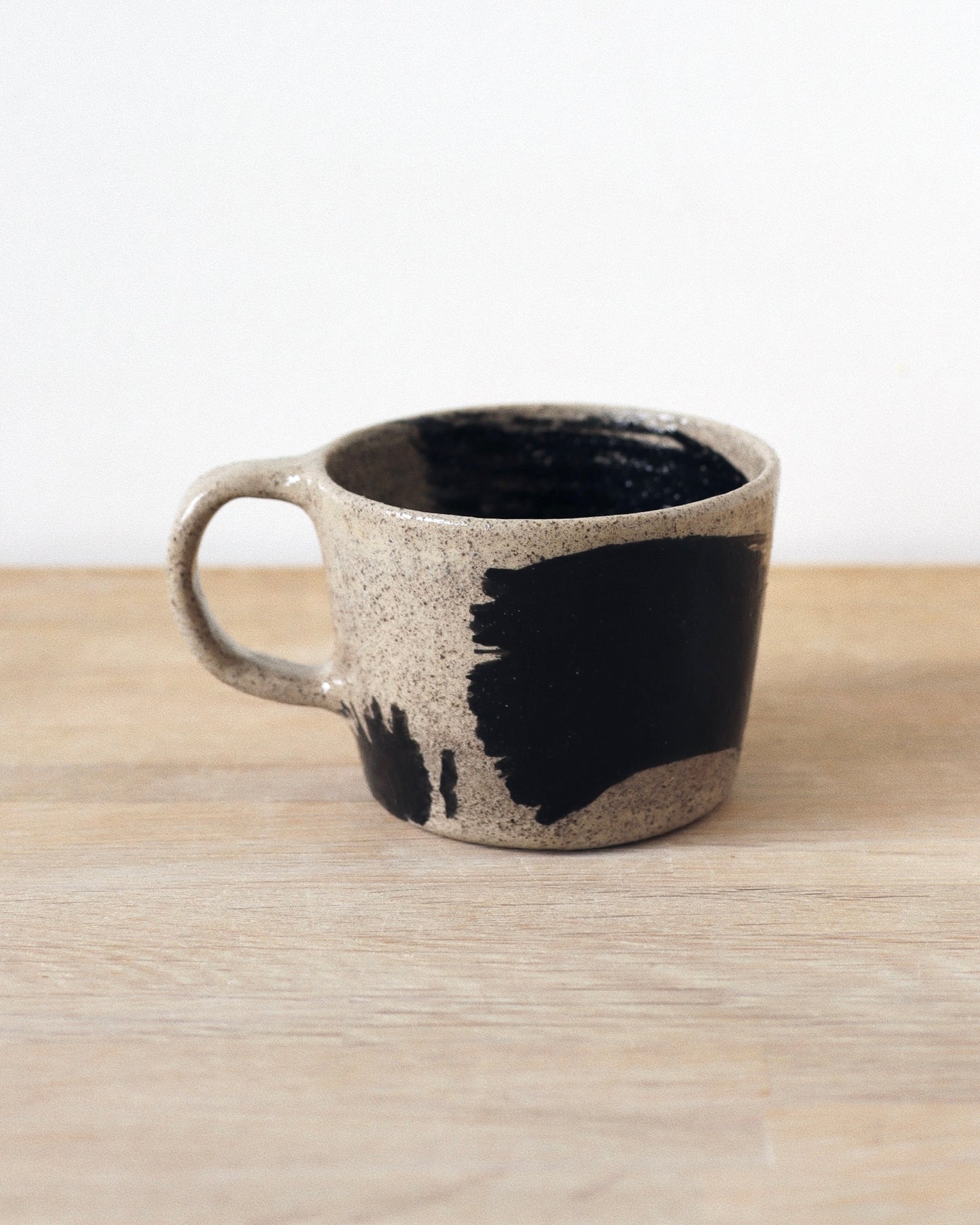 Grey Brush-Stroked Cup – handmade grey speckled stoneware cup with black brushstrokes and clear glaze revealing groggy texture, crafted in Amsterdam.