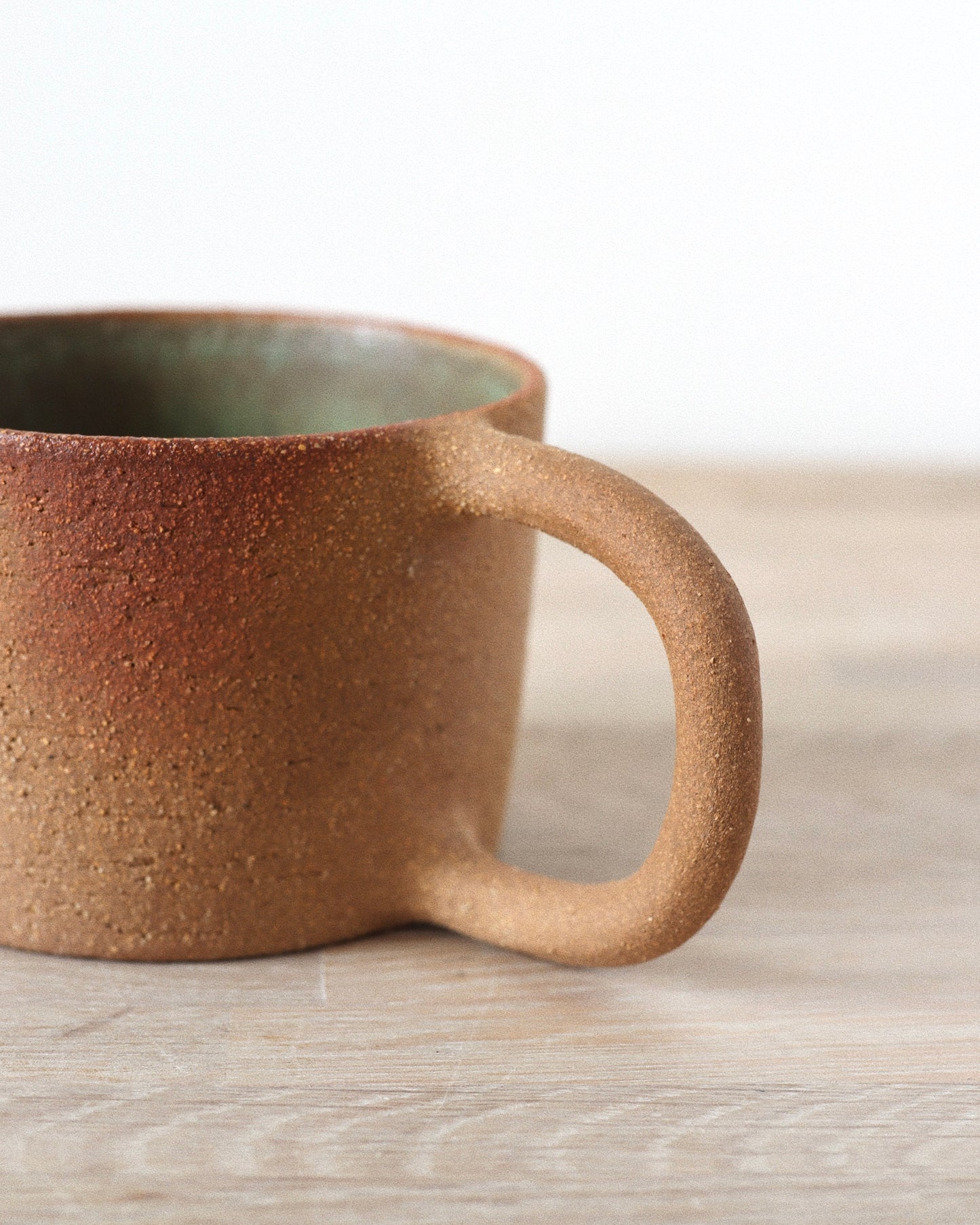 Rhea Mug – handmade red grogged stoneware mug with textured unglazed exterior and deep green glazed interior, crafted in Amsterdam by Zeyah Ceramics.