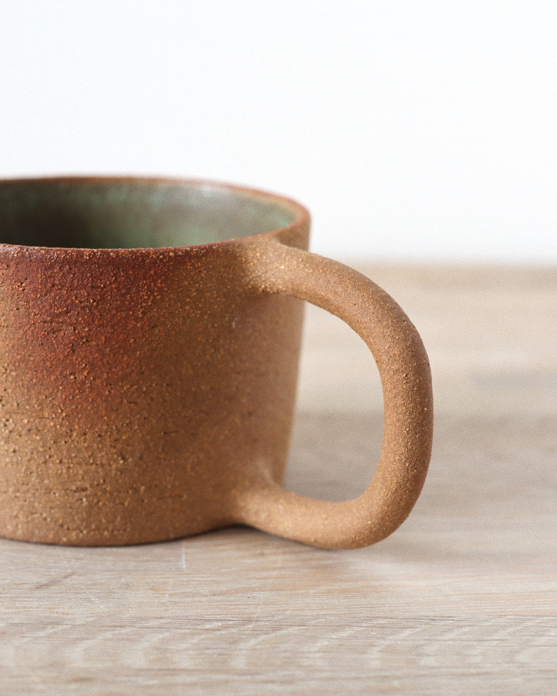 Rhea Mug – handmade red grogged stoneware mug with textured unglazed exterior and deep green glazed interior, crafted in Amsterdam by Zeyah Ceramics.