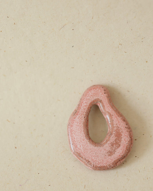 Light grey, hand-formed speckled stoneware amulet finished with a rose quartz colored glaze, showing subtle speckling and smooth contours.